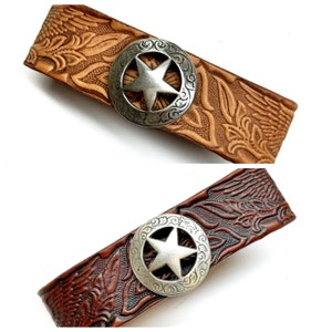May include: Two leather bracelets featuring a silver star design. The bracelets are brown and tan with a floral pattern.