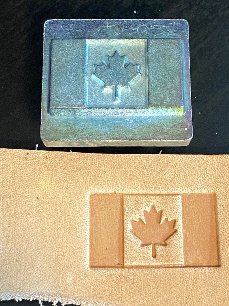 May include: A metal stamp with a design of the Canadian flag. The stamp is used to create an impression of the flag on leather.
