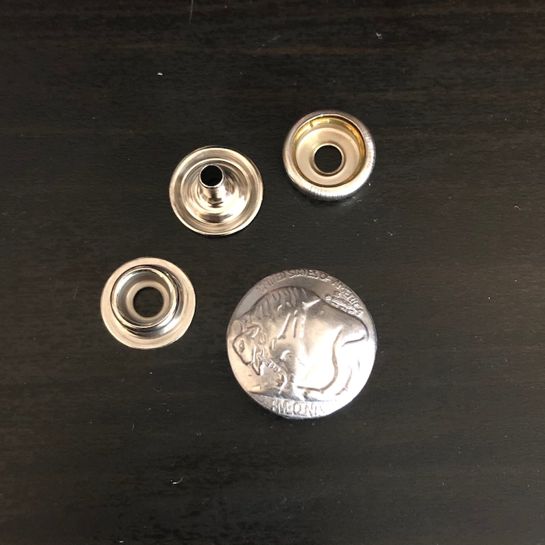 Puede incluir: Cuatro botones a presi&oacute;n de metal plateado, uno con un dise&ntilde;o en relieve de un b&uacute;falo y tres con una superficie lisa.