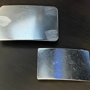 May include: Two silver metal belt buckles, one rectangular and one curved, both with a brushed finish.