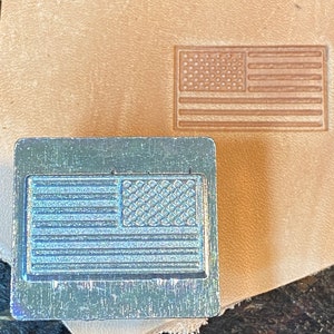 May include: A metal stamp with a design of the American flag. The stamp is used to create impressions on leather.