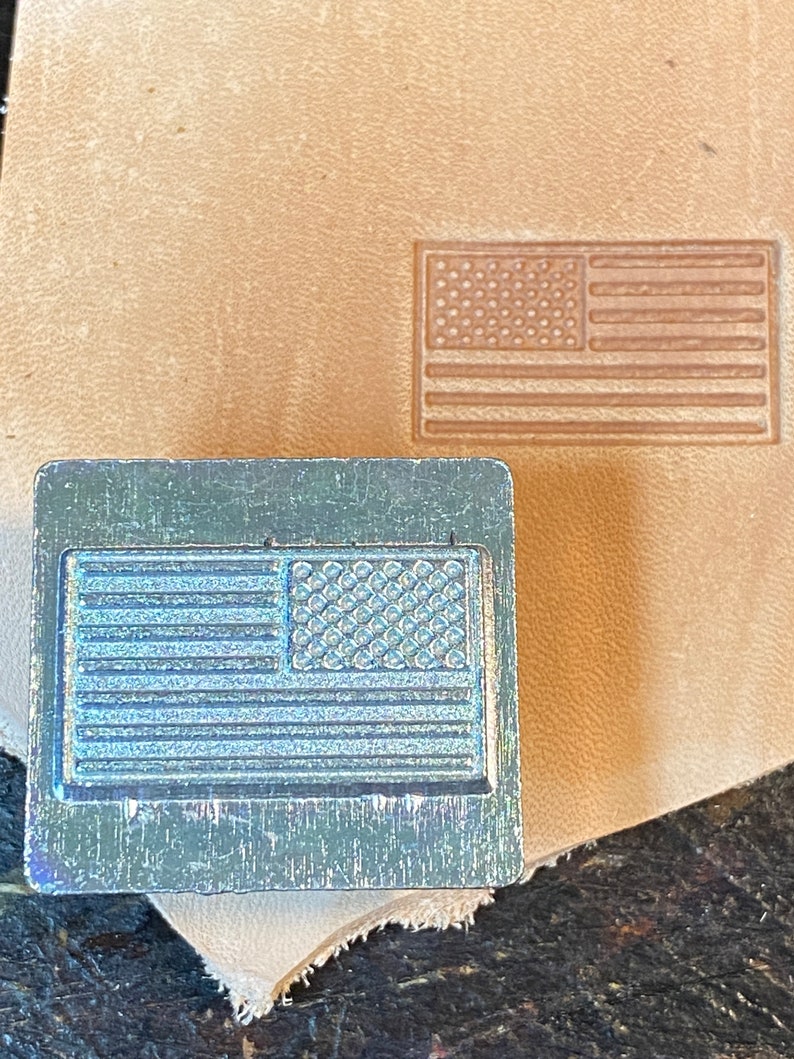 May include: A metal stamp with a design of the American flag. The stamp is used to create impressions on leather.