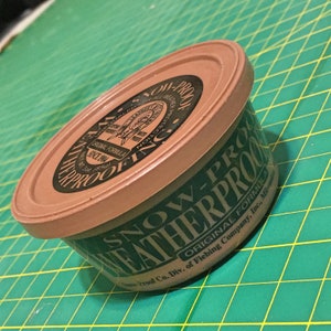 May include: A brown plastic container with a green label that reads "SNOW-PROOF WEATHERPROOF ORIGINAL FORMULA Fiebing Company, Inc., Milwaukee, WI".