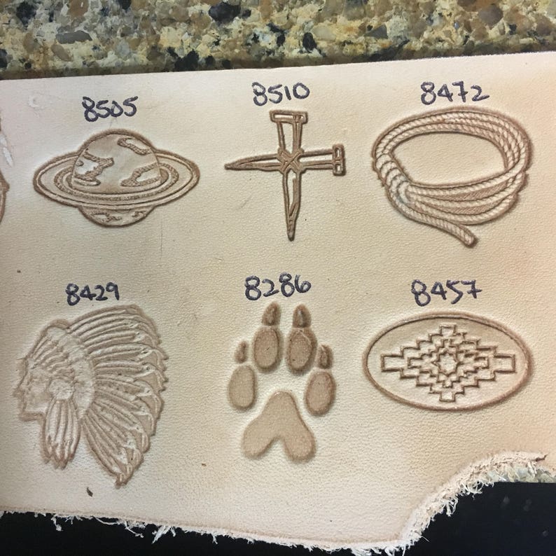 May include: A close-up of a leather surface with various leather stamping designs. The designs include a planet, a nail, a rope, a headdress, a paw print, and a geometric pattern. Each design is labeled with a number.