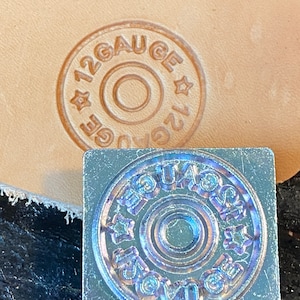 May include: A close-up of a metal stamp with the words "12 Gauge" engraved in a circle. The stamp is used to create impressions on leather.