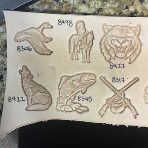 May include: A sheet of leather with various designs embossed on it, including a duck, a Native American on horseback, a tiger, a wolf, a fish, and two crossed rifles. The designs are numbered with the following numbers: 8306, 8498, 8427, 8317, 8422, 8345.