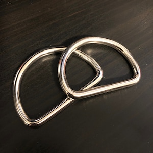 May include: Two silver metal D-rings, one slightly larger than the other, are stacked on top of each other. The rings are smooth and shiny.