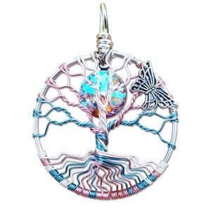 Peut inclure: Un pendentif en fil de fer en forme d'arbre de vie avec un cristal bleu et vert au centre et un charme papillon argenté. L'arbre est fait de fil de cuivre et présente un motif en spirale rose et blanc.