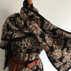 May include: A black and brown floral patterned scarf with a black border. The scarf is draped over a mannequin and tied around the neck. A brown leather belt with a small pouch is worn over the scarf.