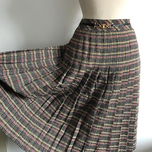 May include: A black, yellow and red plaid skirt with a gold buckle belt. The skirt is pleated and midi length.