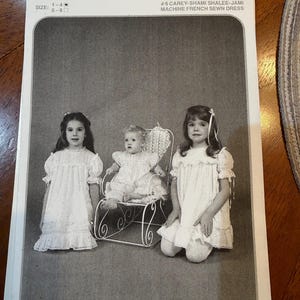 Pode incluir: Imagem a preto e branco de um padrão de costura para um vestido costurado à máquina. O padrão mostra três meninas a usar o vestido. O texto no padrão diz "Briar Patch Designs, Inc." e "#6 CAREY-SHAMI SHALEE-JAMI MACHINE FRENCH SEWN DRESS."