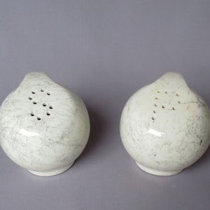 May include: Two white ceramic salt and pepper shakers with a speckled gray glaze and a row of holes on the top.
