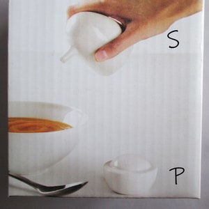 May include: A white ceramic salt shaker is being used to season a bowl of orange soup. A small white bowl with a lid and a spoon are also present. The letter "S" is written on the image, and the letter "P" is written on the image.
