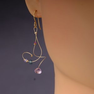 May include: Gold dangle earrings with a purple gemstone and smaller blue and purple gemstones. The earrings are made with wire and have a delicate, abstract design.