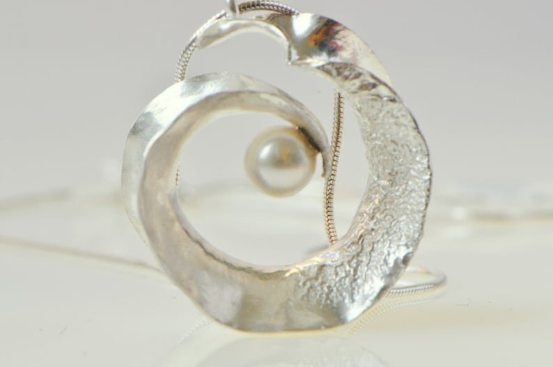 Anticlastic three-dimensional spiral pendant in sterling silver with white freshwater pearl