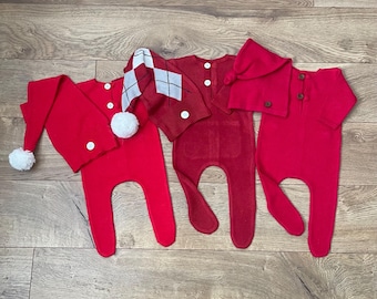 May include: Three red knitted baby outfits with white accents. One outfit has a white pom-pom hat, another has a white and red argyle hat, and the third has a red hood.