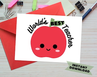 以下が含まれることがあります： 白いカードに黒い文字で「World's Best Teacher」と書かれています。カードの中央には、緑色の茎と笑顔の顔をした赤いリンゴがあります。