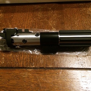 Könnte beinhalten: Ein schwarzer und silberner Lichtschwert-Prop mit einem schwarzen Griff und einer silbernen Klinge. Das Lichtschwert befindet sich in einer durchsichtigen Plastiktüte.