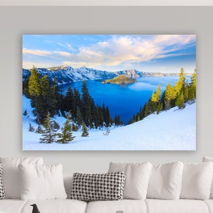 May include: A panoramic view of Crater Lake in Oregon, with snow-capped mountains in the background and a blue lake in the foreground. The lake is surrounded by evergreen trees and a snowy landscape.