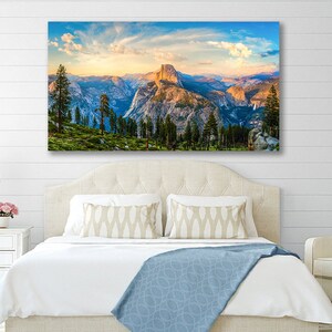 May include: A panoramic view of a mountain range with a large rock formation in the center. The sky is a vibrant blue with fluffy white clouds. The mountains are a mix of brown, green, and gray. There are trees in the foreground.