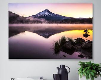 May include: A scenic photograph of a mountain reflected in a still lake at sunrise. The mountain is covered in snow and the sky is a vibrant mix of pink, orange, and yellow. The lake is calm and the water is a deep blue.