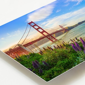 K&ouml;nnte beinhalten: Eine Ansicht der Golden Gate Bridge in San Francisco, Kalifornien. Die Br&uuml;cke ist rot und hat auf jeder Seite einen gro&szlig;en Turm. Die Br&uuml;cke verl&auml;uft &uuml;ber ein Gew&auml;sser und im Hintergrund befinden sich gr&uuml;ne H&uuml;gel. Der Himmel ist blau mit wei&szlig;en Wolken.