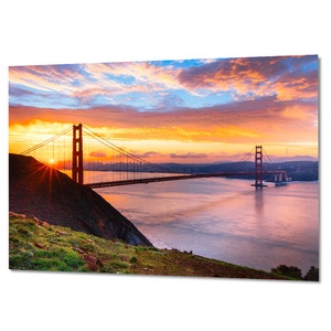 K&ouml;nnte beinhalten: Ein Panoramablick auf die Golden Gate Bridge in San Francisco, Kalifornien. Die Br&uuml;cke ist vor einem leuchtend orangefarbenen und rosafarbenen Sonnenaufganghimmel silhouettiert. Das Wasser unter der Br&uuml;cke ist ruhig und spiegelt die Farben des Himmels wider.