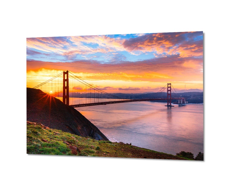 K&ouml;nnte beinhalten: Ein Panoramablick auf die Golden Gate Bridge in San Francisco, Kalifornien. Die Br&uuml;cke ist vor einem leuchtend orangefarbenen und rosafarbenen Sonnenaufganghimmel silhouettiert. Das Wasser unter der Br&uuml;cke ist ruhig und spiegelt die Farben des Himmels wider.