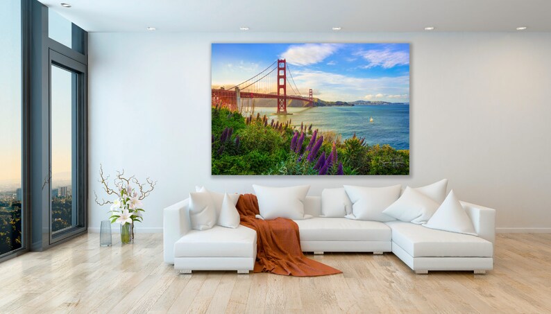 K&ouml;nnte beinhalten: Ein Panoramafoto der Golden Gate Bridge in San Francisco, Kalifornien. Die Br&uuml;cke ist rot und &uuml;berspannt ein Gew&auml;sser mit blauem Himmel und wei&szlig;en Wolken im Hintergrund. Im Vordergrund sind gr&uuml;nes Gras und lila Blumen zu sehen.