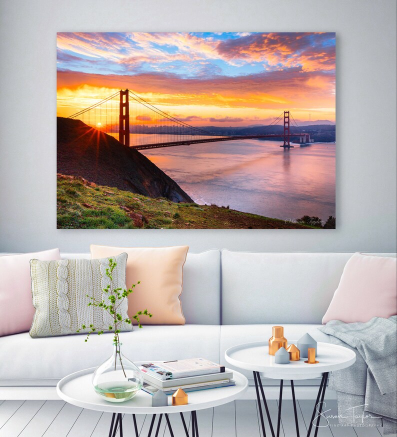 K&ouml;nnte beinhalten: Ein Panoramablick auf die Golden Gate Bridge in San Francisco, Kalifornien. Die Br&uuml;cke ist vor einem leuchtend orangefarbenen und rosafarbenen Sonnenuntergangshimmel mit fluffigen Wolken silhouettiert. Die Sonne geht hinter der Br&uuml;cke unter und wirft einen warmen Schein auf das Wasser.