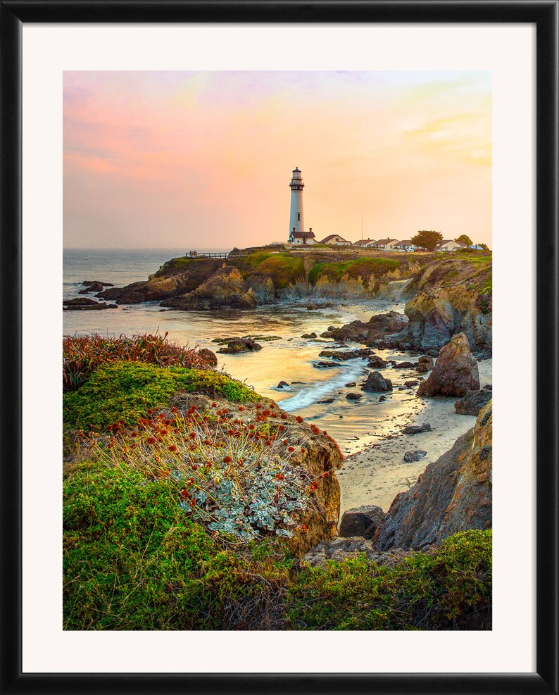 May include: A white lighthouse stands tall on a rocky cliff overlooking a calm ocean. The sky is a vibrant mix of pink, orange, and purple, creating a beautiful sunset scene.