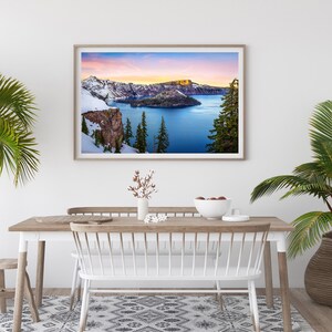 May include: A framed photograph of Crater Lake in Oregon, featuring a snow-capped mountain range, a blue lake, and a small island in the center. The sky is a vibrant pink and orange at sunset.