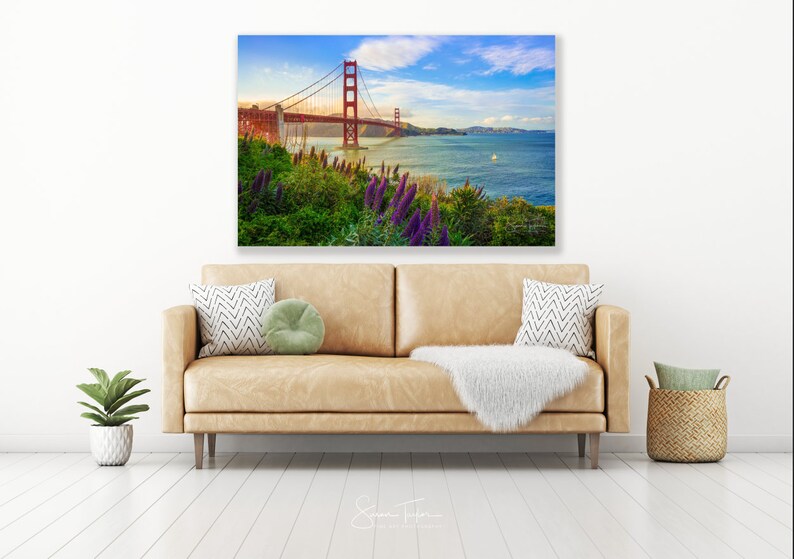 K&ouml;nnte beinhalten: Ein Foto der Golden Gate Bridge in San Francisco, Kalifornien. Die Br&uuml;cke ist rot und &uuml;berspannt ein Gew&auml;sser. Das Wasser ist blau und im Hintergrund befinden sich gr&uuml;ne H&uuml;gel. Im Vordergrund befinden sich lila Blumen.