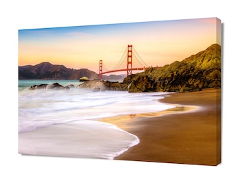 May include: A scenic view of the Golden Gate Bridge in San Francisco, California. The bridge is red and spans a body of water with a sandy beach in the foreground. The water is a light blue and white, with waves crashing on the shore. The sky is a light blue and orange, with clouds in the distance.