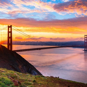 K&ouml;nnte beinhalten: Eine malerische Aussicht auf die Golden Gate Bridge in San Francisco, Kalifornien. Die Br&uuml;cke ist vor einem leuchtend orangefarbenen und rosafarbenen Sonnenaufganghimmel silhouettiert. Die Sonne scheint hell hinter der Br&uuml;cke und erzeugt einen Sterneneffekt.