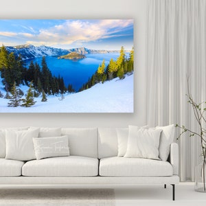 May include: A panoramic view of Crater Lake in Oregon, with snow-covered hills and a blue lake in the background. The lake is surrounded by trees and mountains. The sky is blue with white clouds.