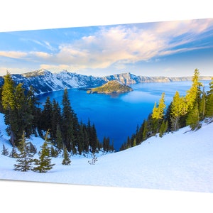 May include: A panoramic view of Crater Lake in Oregon, with snow-capped mountains and a deep blue lake. The lake is surrounded by a lush forest of evergreen trees. The sky is a bright blue with white clouds.