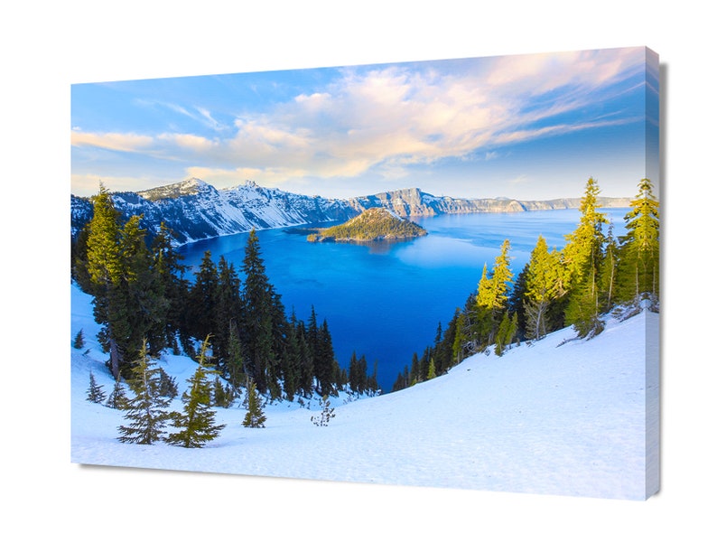 May include: A panoramic view of Crater Lake in Oregon, with snow-capped mountains and a deep blue lake. The lake is surrounded by a lush forest of evergreen trees. The sky is a bright blue with white clouds.
