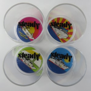 Pode incluir: Quatro copos de plástico transparente com um disco giratório dentro de cada um. Os discos têm um fundo azul com um navio branco e o texto "steady as she goes" em preto.