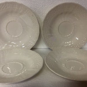 Puede incluir: Cuatro platillos de cerámica blanca con un diseño en relieve. Los platillos tienen un hueco central para sostener una taza.