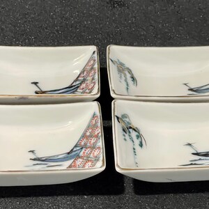 Puede incluir: Juego de cuatro platos pequeños de cerámica blanca con borde dorado. Cada plato presenta un diseño pintado a mano de un barco con un sauce llorón y flores rojas y blancas.