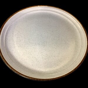 May include: A white ceramic dinner plate with a brown rim. The plate has a speckled texture.