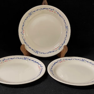 Puede incluir: Tres cuencos de cerámica blanca con diseños florales azules y rosas. Los cuencos están apilados uno encima del otro.