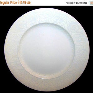May include: White ceramic dinner plate with a raised, embossed design of a floral pattern around the edge.