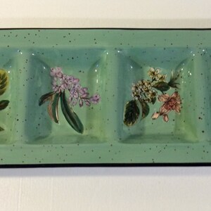 Könnte beinhalten: Ein rechteckiges Serviertablett aus Keramik mit vier unterteilten Abschnitten. Jeder Abschnitt zeigt ein anderes Blumenmuster, das in Grün-, Weiß-, Rosa- und Rottönen bemalt ist.