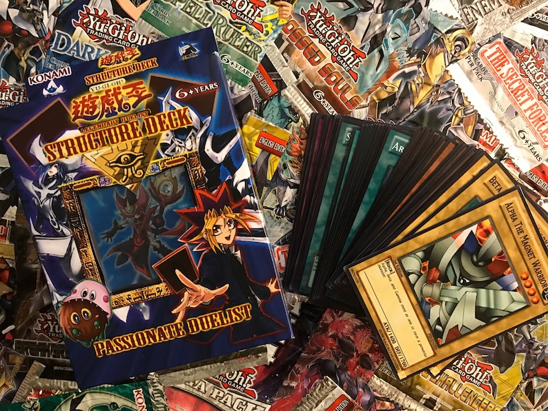 Puede incluir: Una caja de Deck de Estructura Yu-Gi-Oh! azul y roja con el texto "Structure Deck" y "Passionate Duelist". La caja presenta una ilustraci&oacute;n de un personaje de la serie de anime Yu-Gi-Oh!. La caja est&aacute; rodeada de una variedad de cartas de intercambio Yu-Gi-Oh!