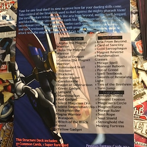 Puede incluir: Un dorso de carta azul y negro con una imagen de un guerrero sosteniendo una espada. El dorso de la carta tiene texto que dice "Time for one final duel! It's time to prove how far your dueling skills come. Take control of the final deck used to duel against the mighty pharaoh Atem!" y "This Structure Deck includes: 37 Common Cards, 1 Super Rare Card, 1 Ultra Rare Card, and 1 Secret Rare Card!"