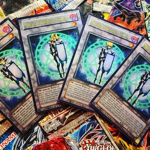 Puede incluir: Cuatro cartas coleccionables que presentan el Token Caballero Espejo del Juego de Cartas Coleccionables Yu-Gi-Oh! Cada carta tiene un fondo azul y verde con un personaje guerrero que sostiene un escudo. El texto en las cartas dice "Token Caballero Espejo" y "Edición Limitada".