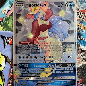 May include: A holographic Pokemon trading card featuring Milotic GX, a water-type Pokemon with a pink hat and blue hair. The card has a light blue background with silver glitter. The card text reads "Mystic Scale", "Hypno Splash", and "Summer Days GX".