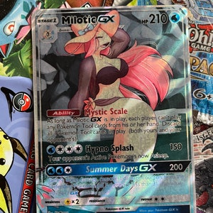 May include: A holographic Pokemon trading card featuring Milotic GX, a pink and blue water-type Pokemon with a large, flowing tail. The card has a blue background with white text and stars. The card's text includes the Pokemon's name, HP, abilities, and attacks. The card is in excellent condition.